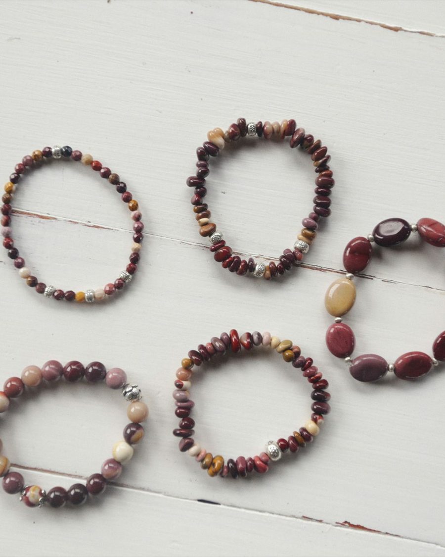 Assorted red, brown, and stone-toned beaded bracelets on white wood