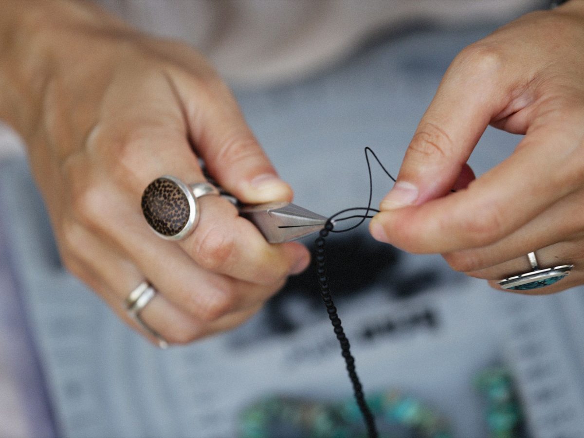 A craftsperson's hands threading small beads at a worktable