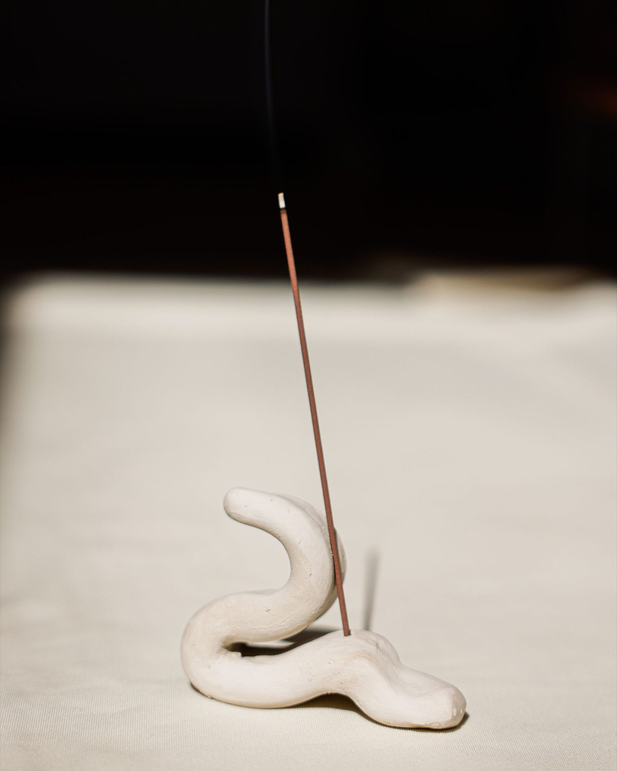 A slender incense stick standing in a sculptural white ceramic holder