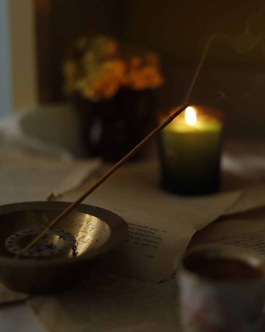 A glowing candle and incense resting beside an open book in evening light